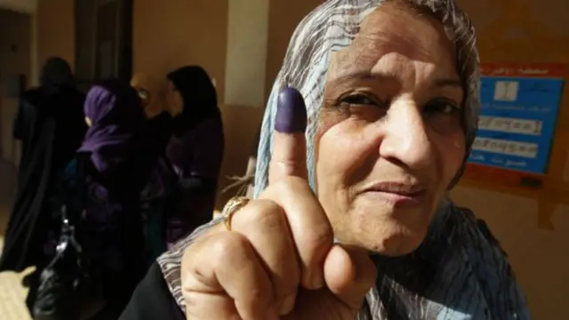 A Libyan woman displays the ink on her finger after casting her vote