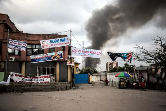 Electoral banners are seen as smoke rises from a fire at the independent national electoral commission"s (CENI) warehouse on December 13, 2018 in Kinshasa, ten days ahead of presidential elections that have been foreshadowed by violence.