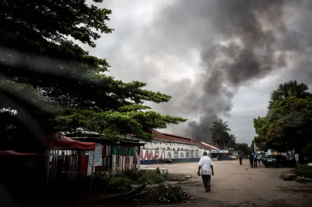 A man walks towards smoke rising from a fire at the independent national electoral commission"s (CENI) warehouse on December 13, 2018 in Kinshasa, ten days ahead of presidential elections that have been foreshadowed by violence.