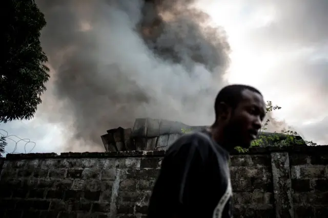 A man walks past smoke rising from a fire at the independent national electoral commission's (CENI) warehouse on December 13, 2018 in Kinshasa, ten days ahead of presidential elections.