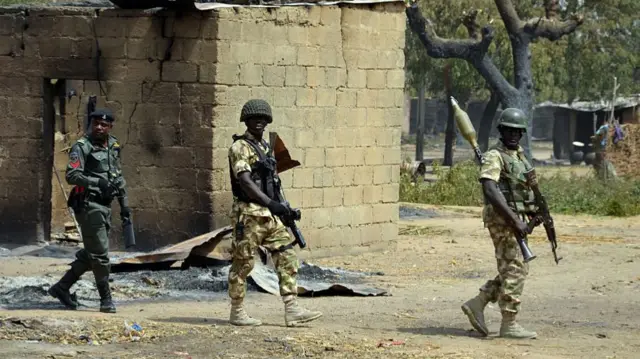 Soldiers and policemen walk past burnt house on February 4, 2016 during a visit to the village of Dalori village, some 12 kilometres from Borno state capital Maiduguri, northeastern Nigeria