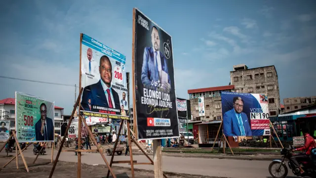 A motorbike taxi drives past campaign posters in the district of Lingwala in Kinshasa, DR Congo