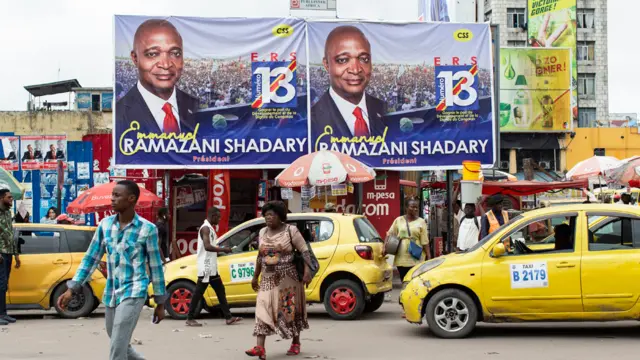 People walk in front of campaign banners of the ruling party candidate Emmanuel Ramazani Shadary in Kinshasa, DR Congo