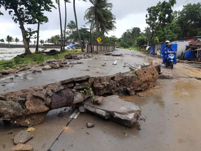 Residents ride a motorcycle past a collapsed wall after the tsunami hit Carita beach in Pandeglang, Banten province