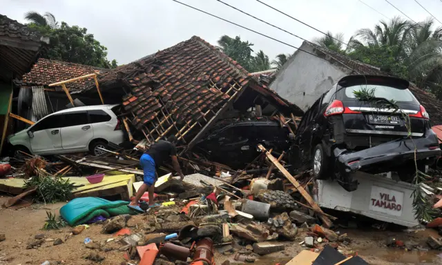 A resident searches for items among the ruins of a villa in Carita beach, Indonesia