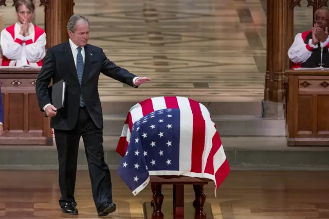 An emotional former President George Bush touches the flag-draped casket of his father