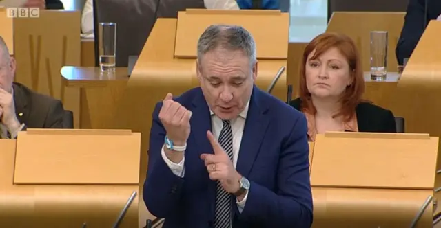 Richard Lochhead is wearing a unity band, proceeds of which are going to CRUK