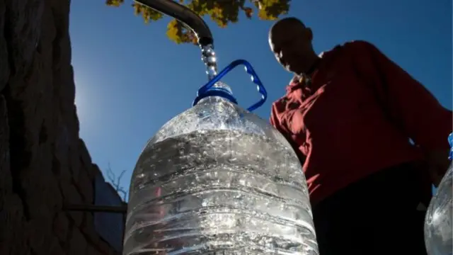 A man fills a large water bottle from a tap