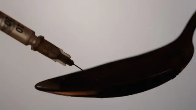 Silhouette of drug addict takes a heroin from the spoon by a syringe