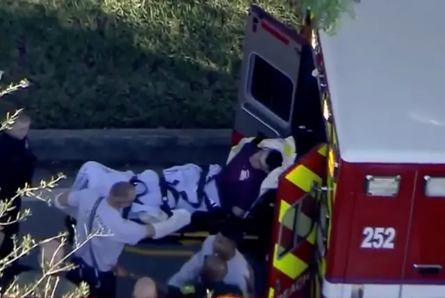 A man who was placed in handcuffs by police is loaded into an ambulance outside the school