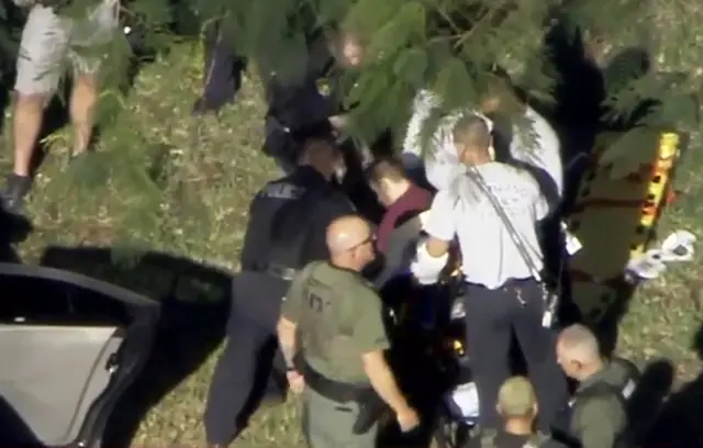 A man placed in handcuffs by police is loaded onto a stretcher in Parkland, Florida.