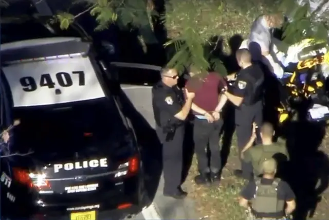 A man placed in handcuffs by police is loaded onto a stretcher in Parkland, Florida.