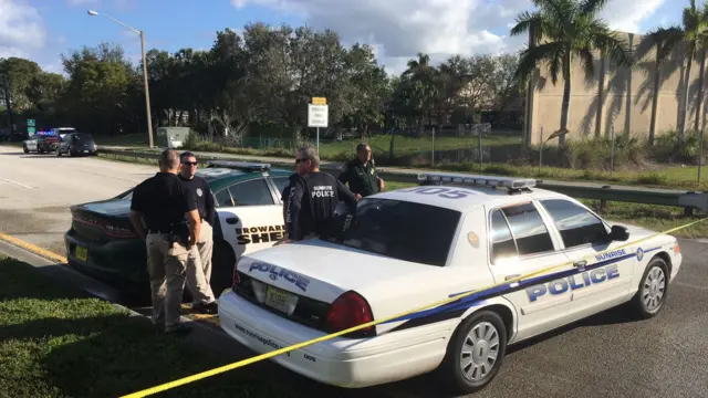 Police officers stand by their cars on a sunny morning at the scene