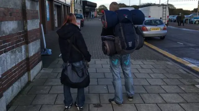 Two homeless people carrying bags.