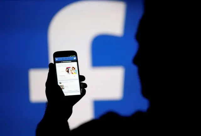 Man holding phone looking at Facebook