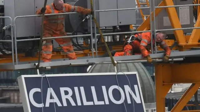 Workers next to Carillion sign