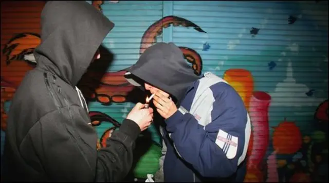 Two boys with their hoods up smoking.