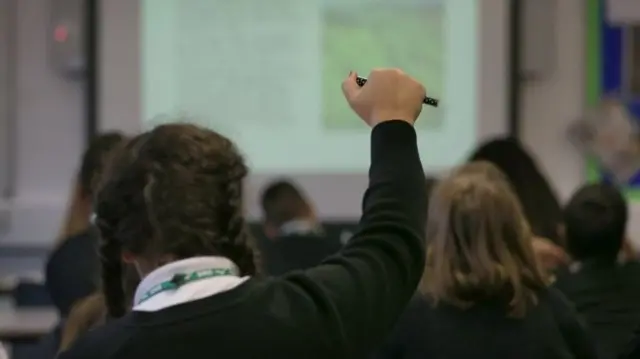 A child in a class holding their hand up.