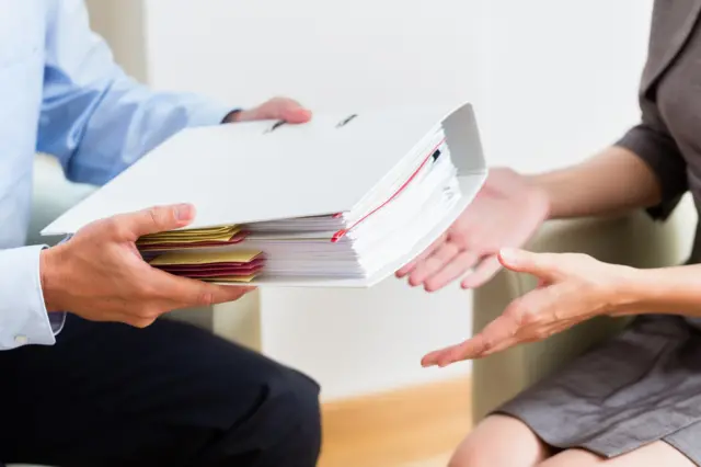 A man handing a folder to a woman