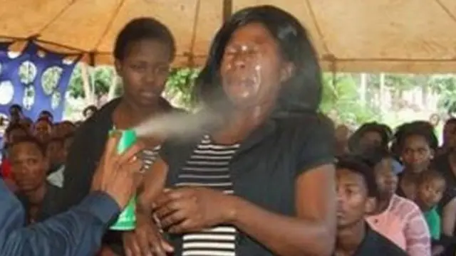 A man spraying insecticide in the face of a woman before a congregation.