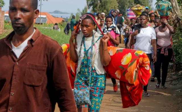 Refugees from the Democratic Republic of Congo carry their belongings as they walk near the United Nations High Commissioner for Refugees (UNHCR) offices in Kiziba refugee camp in Karongi District, Rwanda