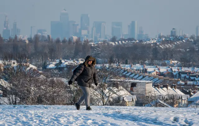 A woman walks over snowy Blythe Hill, in south London