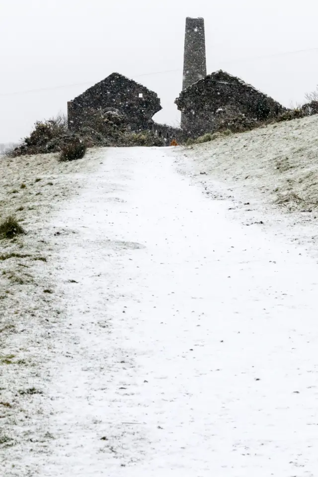 An old mine building behind snow on the ground at Redruth