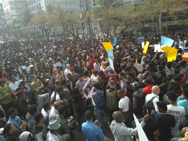 A wide shot showing hundreds of protestors, some holding banners