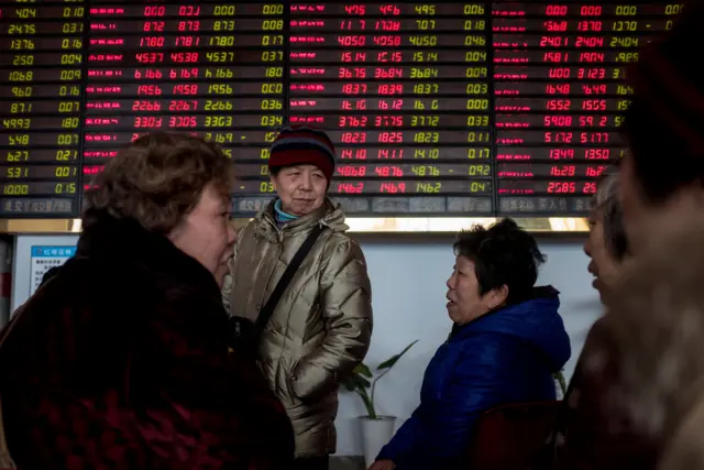 People stand in front of stock market boards in Asia