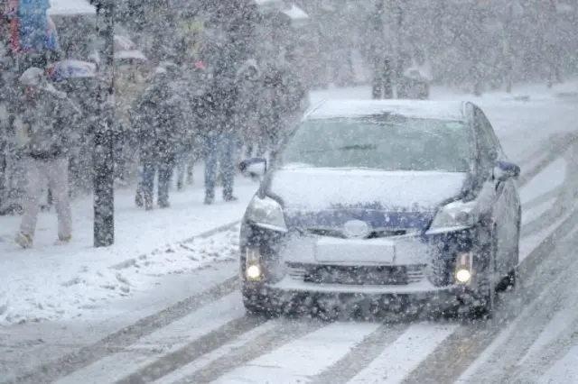 A car drives down a snow-covered street