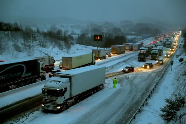 Drivers manoeuvre their cars past stationary lorries on the M80