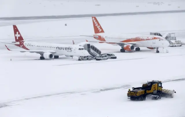 A snow plough removes snow next to EasyJet and Helvetic aircrafts during a temporary closure at Cointrin airport in GenevaA snow plough removes snow next to EasyJet and Helvetic aircrafts during a temporary closure at Cointrin airport in Geneva