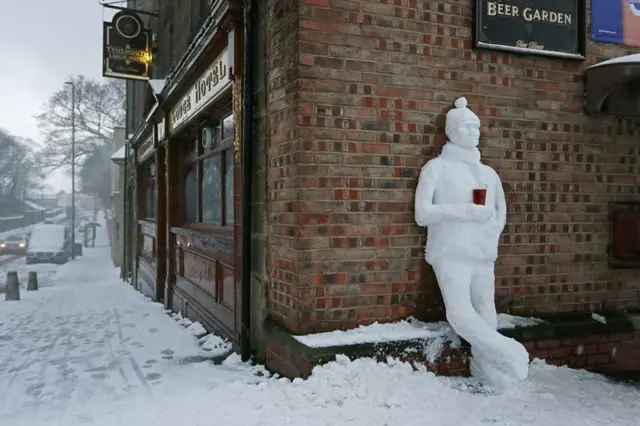 Sculpture of a drinker made from snow against the pub wall