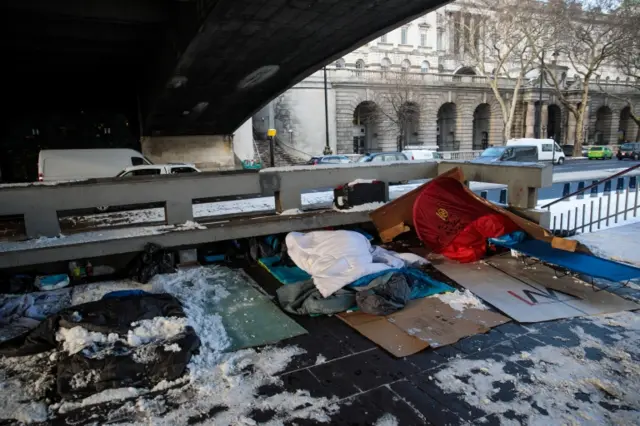 Bedding and shelters belonging to homeless people lie under a bridge covered in snow on the Embankment