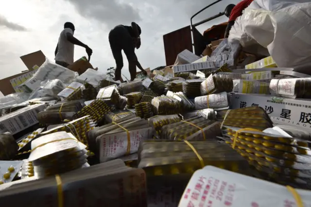 A picture taken at the cemetery of Abobo district of Abidjan on March 10, 2017 shows fake medecine bearing Chinese character as people unload boxes of counterfeit drugs from a truck. 50 tonnes of fake medicine, for an estimated value of more than 1 million euros, were burnt in Abidjan on March 10, 2017.