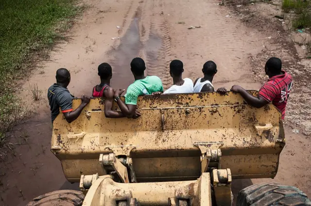 Construction workers ride to their building site in the bucket of a bulldozer.