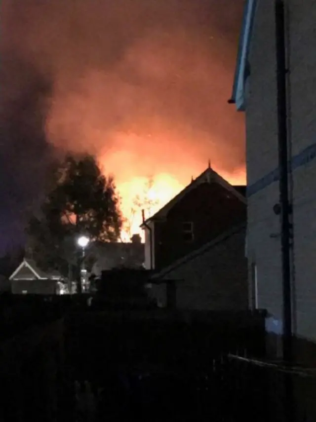 The fire lighting up the night sky behind houses.