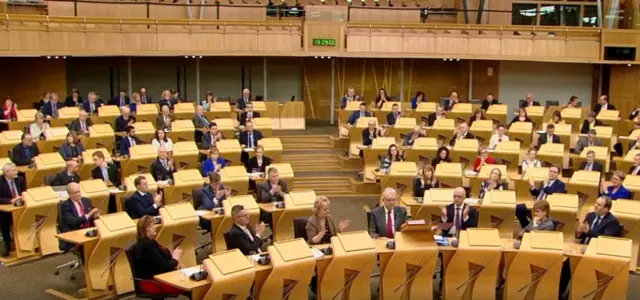 Brexit Minister Mike Russell sits amidst aplauding SNP MSPd