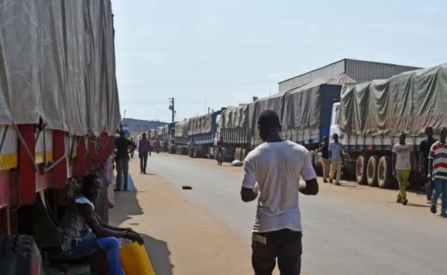 Pedestrians walk past lorries laden with coffee for export at the port of Abidjan on March 8, 2018