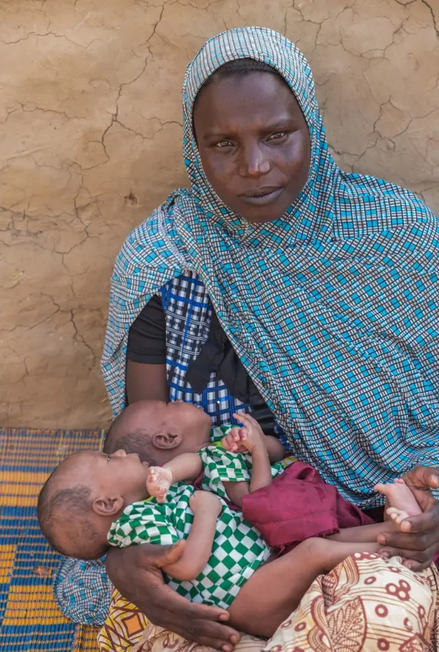 Soumaila Soumana's wife holds two-month-old twins Hassana and Housseina outside their home in Norandé