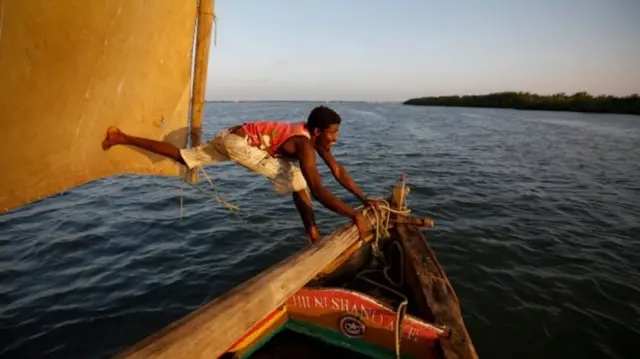 A man adjusts a mast aboard a dhow boat carrying tourists as it sails during the sunset off the coast of Lamu Island, a popular beach resort in Kenya.