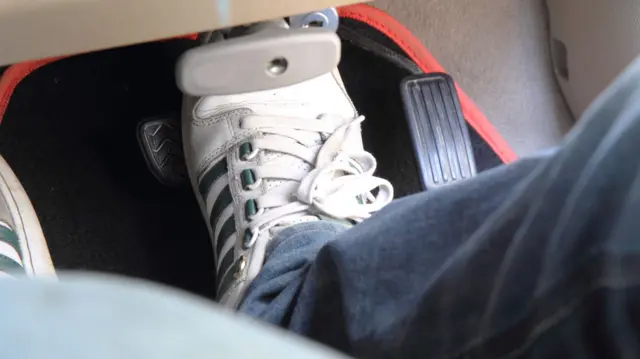 Driver wearing jeans and trainers using pedals in car