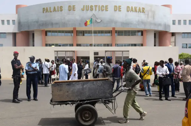 A man pushes a carriage past people and Senegalese security forces members standing outside Dakar Courthouse on May 30, 2016 in the Senegalese capital.