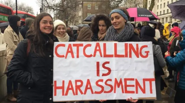 Women with sign saying 'catcalling is harassment'