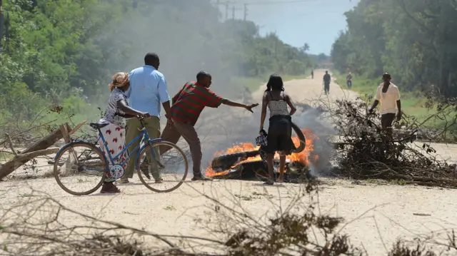 Locals block the road with a barricade as they protest the rising in insecurity following the killings in Mpeketoni