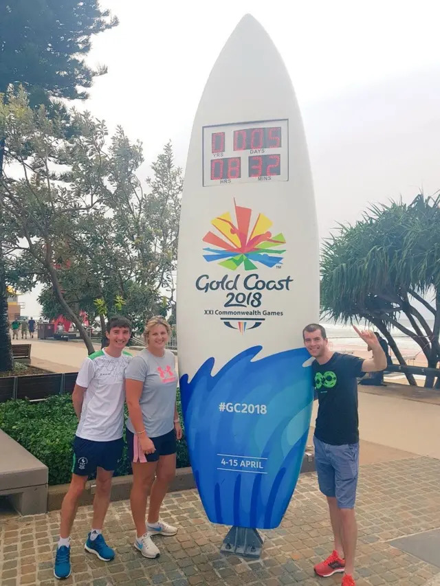 Kevin stands with a giant surf board advertising the games on the Australian Gold Coast