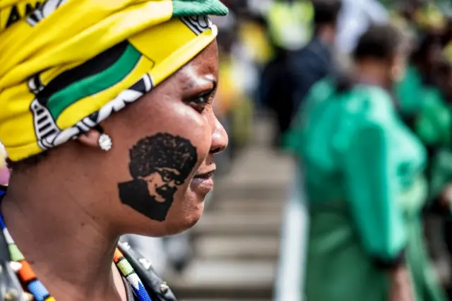 A mourner with a stamp on her cheek featuring late South African anti-apartheid campaigner Winnie Madikizela-Mandela,