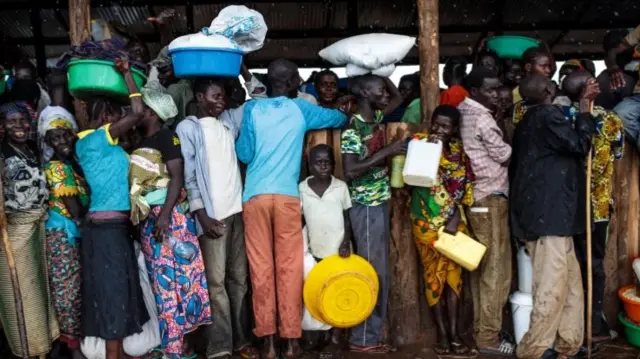 Refugees from the Democratic Republic of Congo stand under a shelter with their food collected from the World Food Programme as it rains in the Kyangwali settlement in Uganda - 10 April 2018