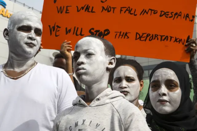 African migrants demonstrate with white paint on their faces, outside the Embassy of Rwanda in the Israeli city of Herzliya on February 7, 2018, against the Israeli government's policy to forcibly deport African refugees and asylum seekers to Rwanda and Uganda.