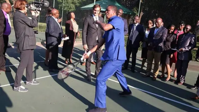 Edgar Lungu playing with a tennis racket - with Roger Federer looking on